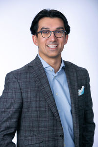 Smiling person in glasses and plaid suit jacket with light blue shirt and pocket square. Background is a soft white gradient. Viewpoint Photography Edmonton