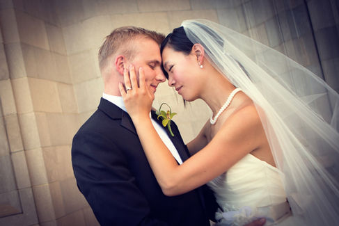 Bride and groom embrace tenderly, eyes closed, in a solemn setting. Bride in white dress with veil; groom in black suit with flower boutonniere. Viewpoint Photography Edmonton