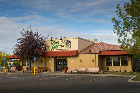 Exterior of Olive Garden restaurant with a beige facade, red roof, and trees. Clear sky. Sign reads "Olive Garden Italian Restaurant." Viewpoint Photography