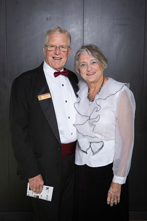 Elderly couple smiling warmly, dressed formally in a tuxedo and white blouse, posing indoors against a dark wood background. Viewpoint Photography Edmonton