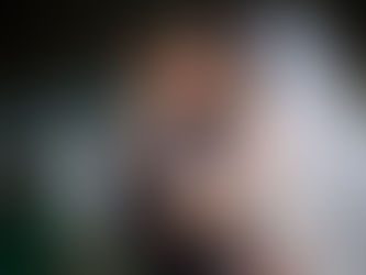 A bride kisses a groom on the cheek as he smiles. A water fountain is in the background. The mood is joyful.