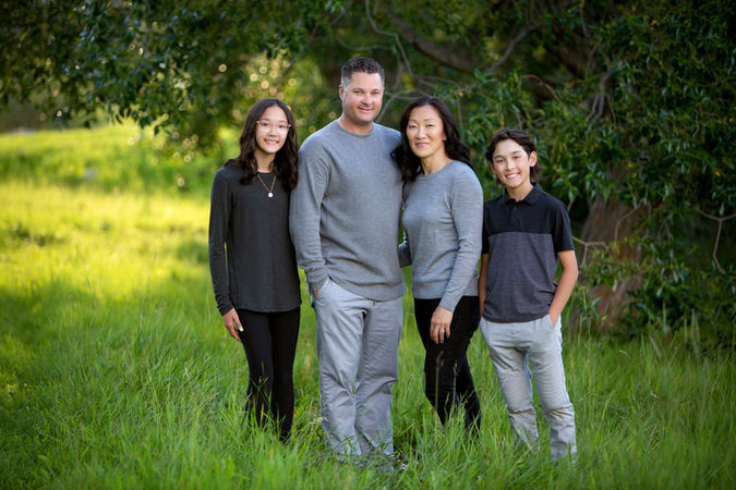 A smiling family of four standing in the park for a photo. Summer photo session Edmonton.