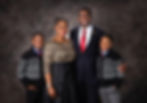 Family portrait with parents and two boys in black patterned sweaters. Parents smile; father wears a red tie. Dark, textured background. Best Edmonton Photographer
