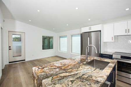 Modern kitchen with a patterned granite island, stainless steel faucet, and appliances. White walls, wooden floor, large windows. Bright ambiance. Viewpoint Photography