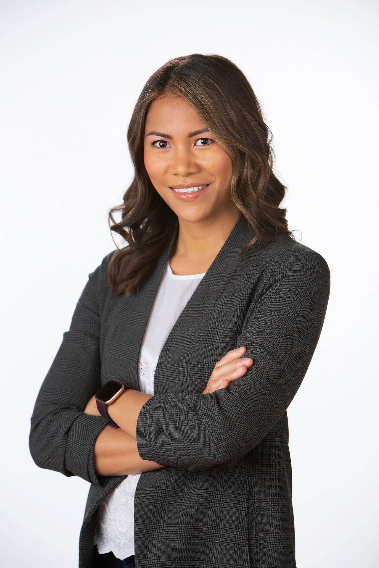 Smiling woman with arms crossed in a gray blazer against a white background. Wears a smartwatch, exuding confidence and professionalism. Viewpoint Photography Edmonton