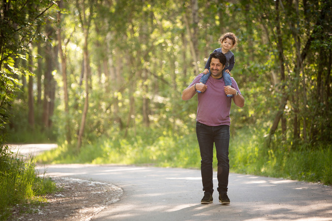 A man carries his young toddler on his shoulders as they walk down a forested trail. The vibe is fun. Viewpoint Photography Edmonton