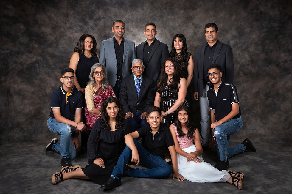 A group of 12 people pose for a family portrait against a dark mottled background. They are dressed formally, smiling, and relaxed. Best Edmonton Photographer