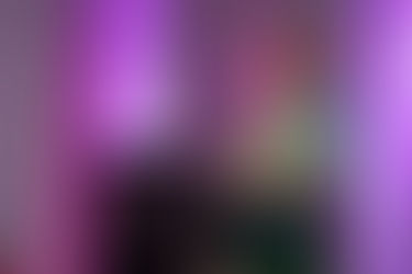 A woman in a colourful shawl speaks at a podium, smiling under pink and purple stage lights with curtains in the background. Viewpoint Photography Edmonton