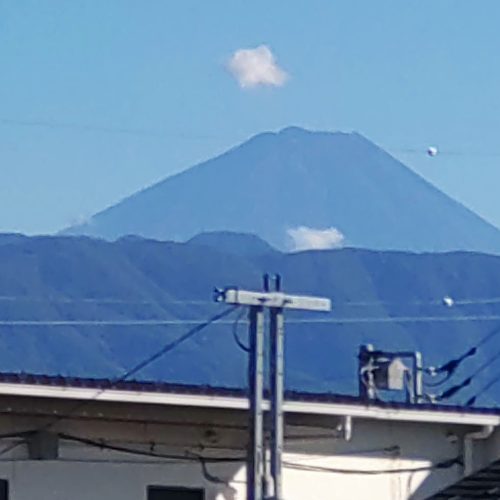 青空の下、遠くに富士山がそびえ、手前に屋根と電柱、白い雲が浮かぶ静かな風景。
