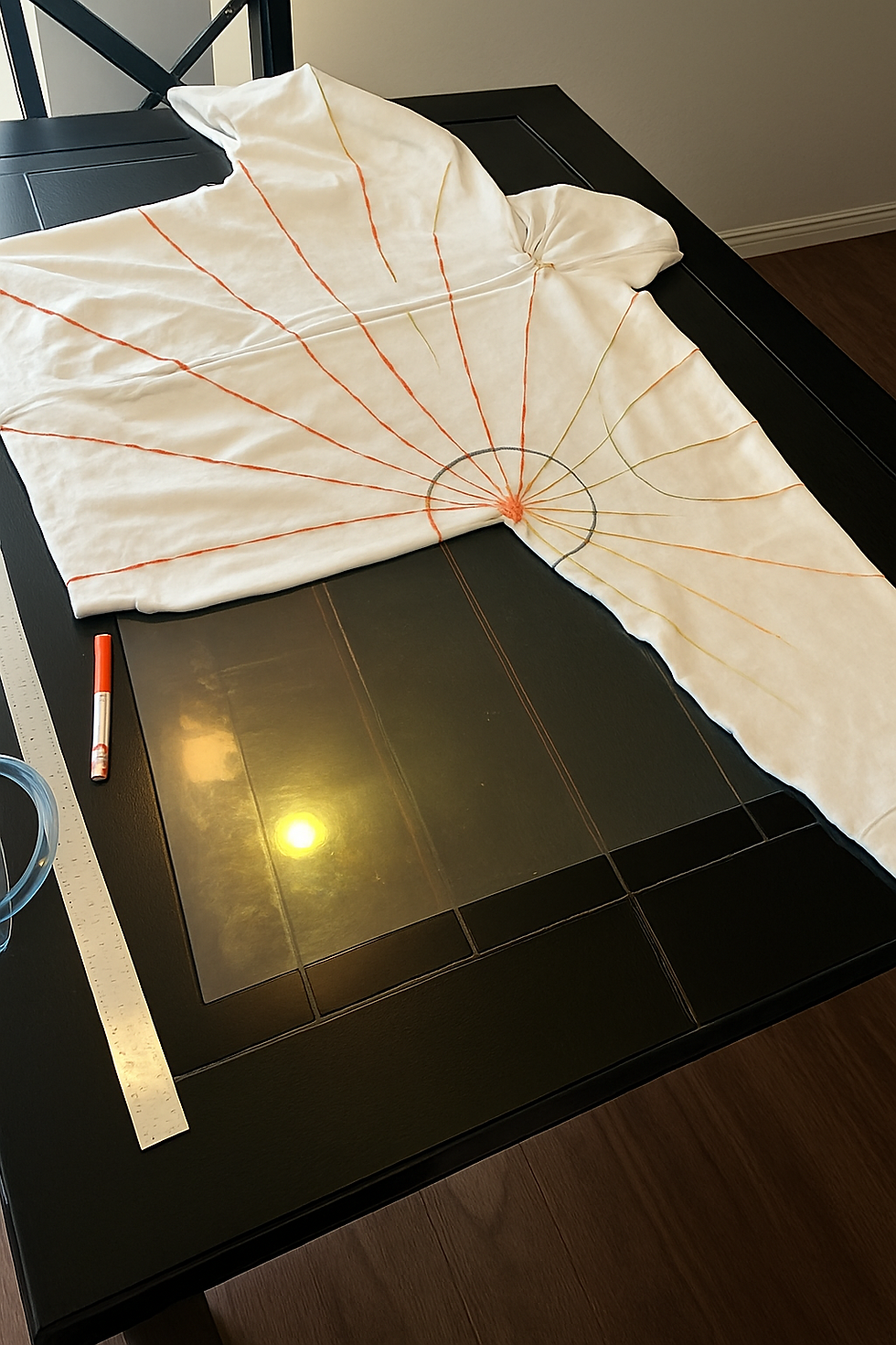 White zip-up hoodie with hand-drawn color burst pattern, prepped for tie-dye on a black glass table.