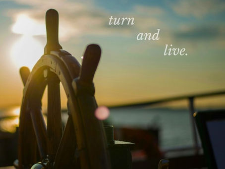 The wheel of a ship, the sun setting over the ocean's horizen
