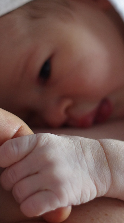 Newborn baby clasping mum's finger