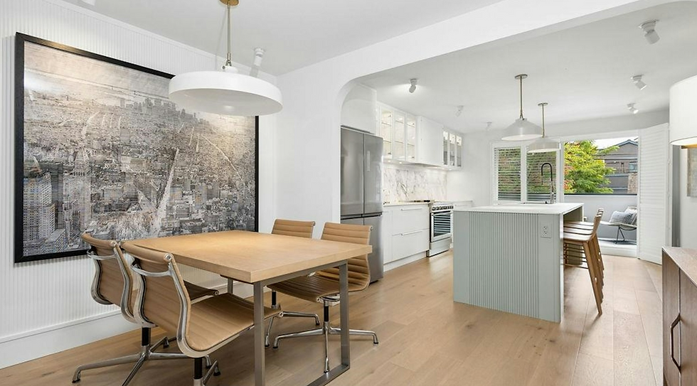 Bright modern kitchen-dining room with wood table, tan chairs, island, stainless appliances, large city wall art, and window seat.