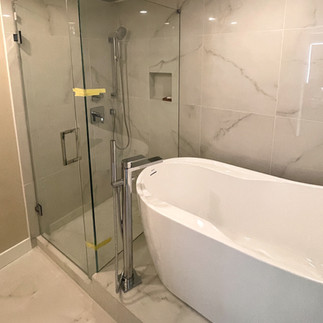 Freestanding bathtub beside glass shower enclosure with marble-look tile walls in modern renovated bathroom