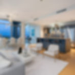 Modern open-concept living room and kitchen with white and gray tones, sleek furniture, and a view of the city through large windows.