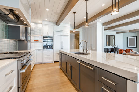 Sleek and stylish modern kitchen featuring white cabinets, a black island, and warm wood floors, with pendant lights casting a cozy glow over a comfortable seating area in the background.