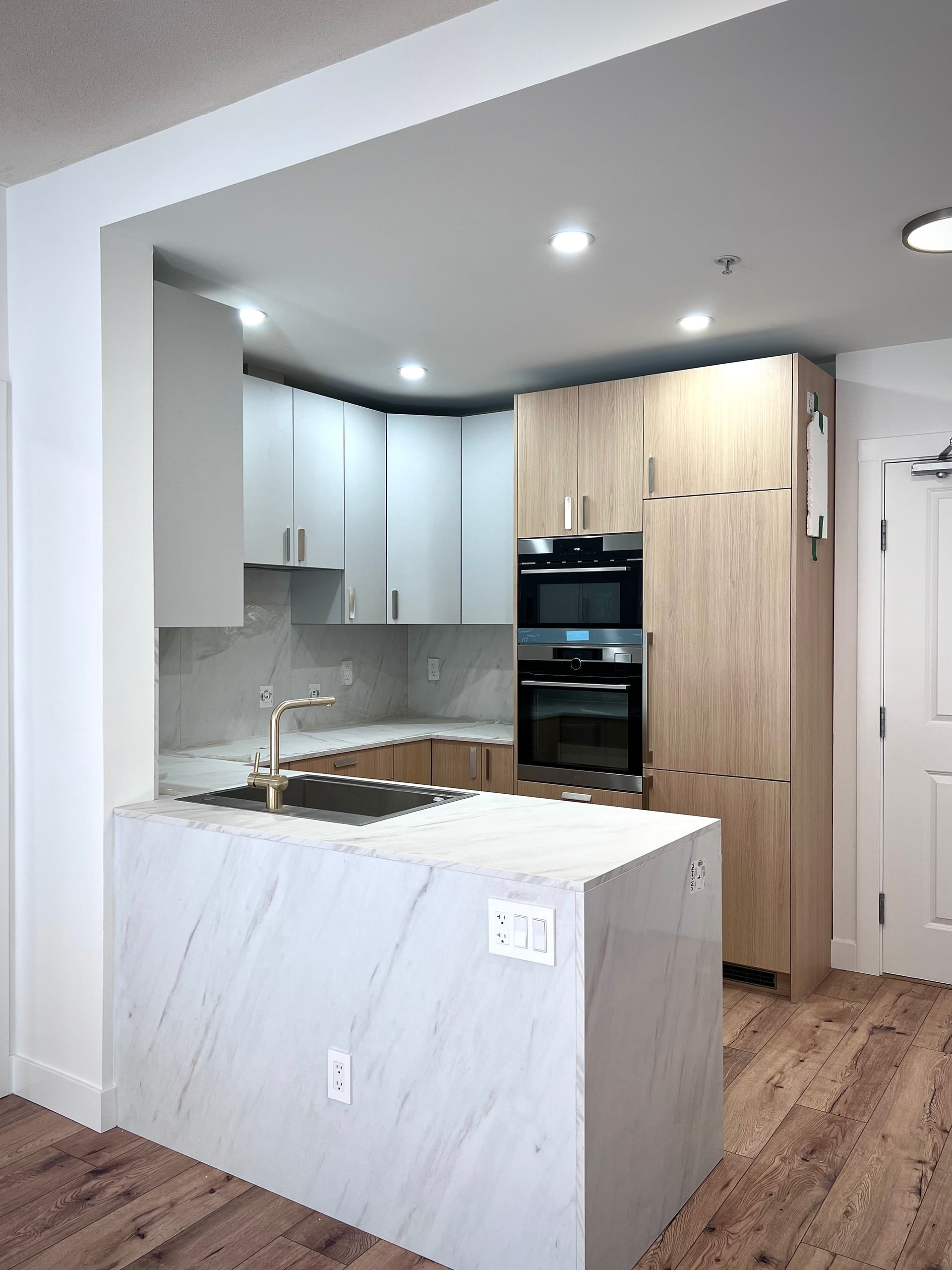 Modern kitchen renovation in North Vancouver featuring white and wood cabinets, quartz countertops, marble backsplash, and recessed lighting