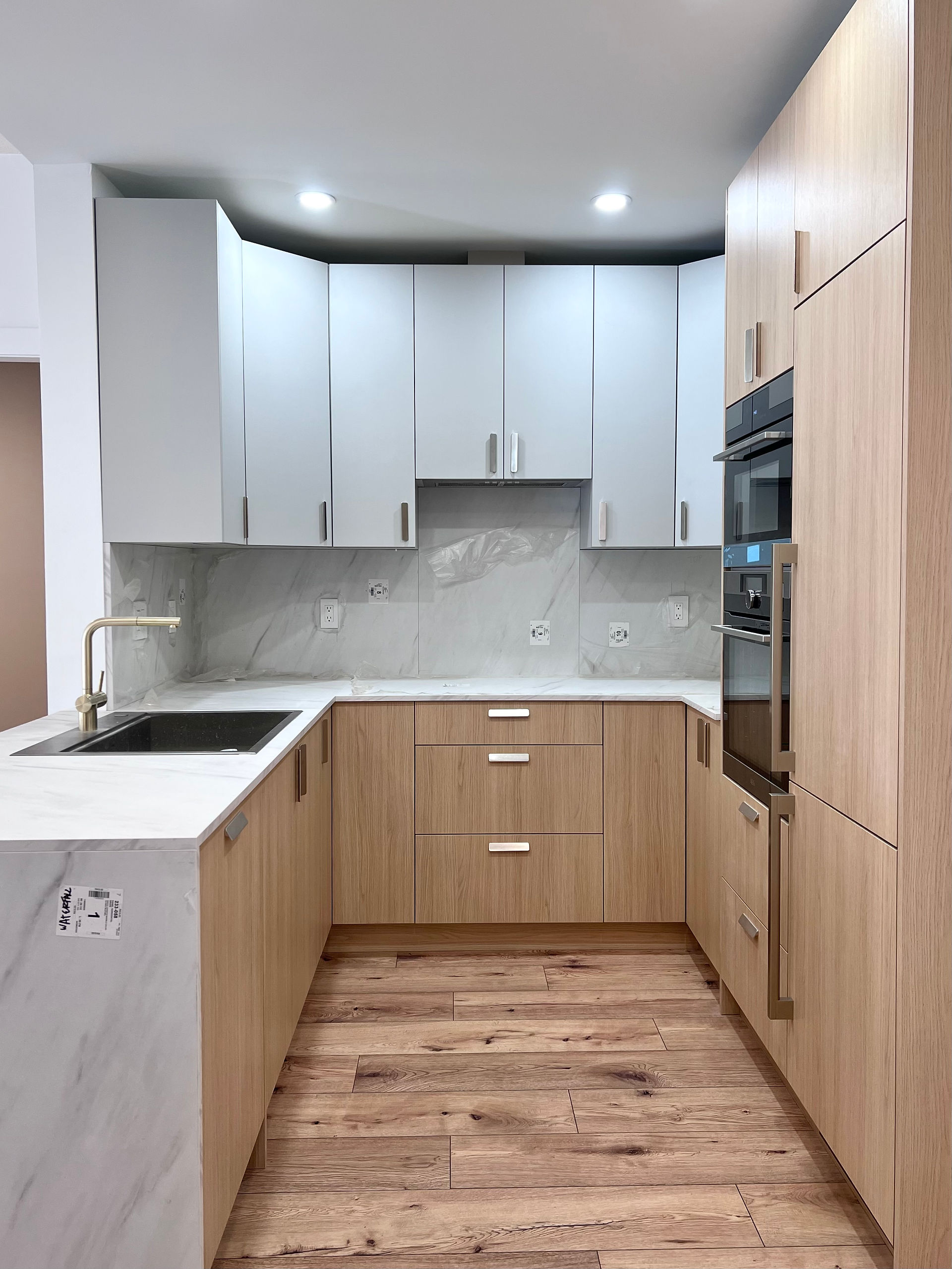 Modern kitchen renovation in North Vancouver with white and wood cabinets, quartz countertops, and new lighting installed by Grand Renovations