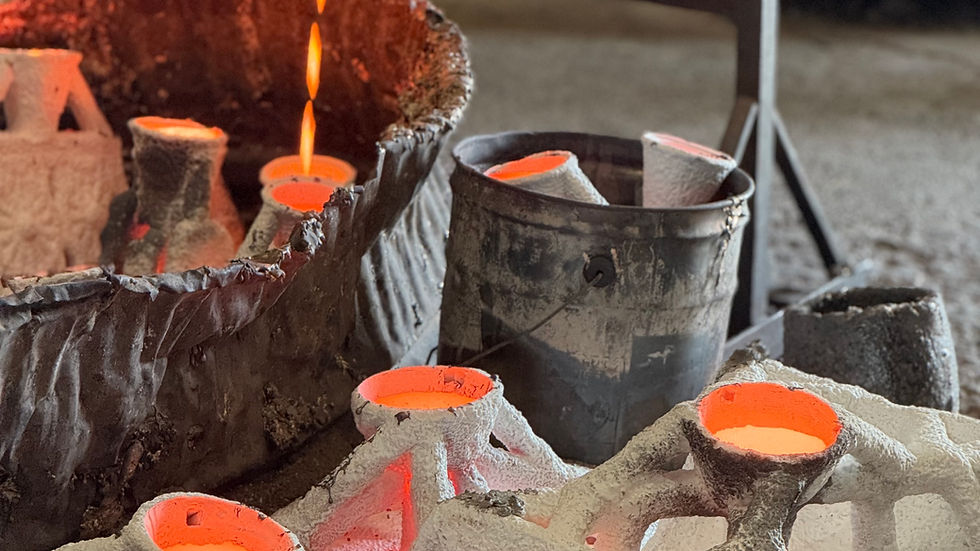 Molten metal pours from a crucible into sand molds, glowing orange in a workshop foundry.