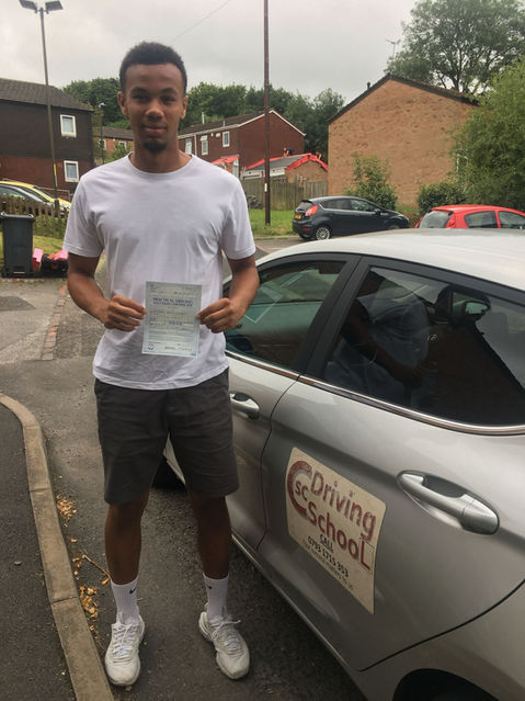 Young boy stood next to a car holding a driving test certificate