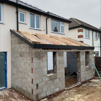 Side view of a brick outhouse with a new extension with pitched roof under construction.