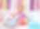 A baby in a purple shirt and rainbow skirt sits beside a pastel blue cake adorned with seashells and stars