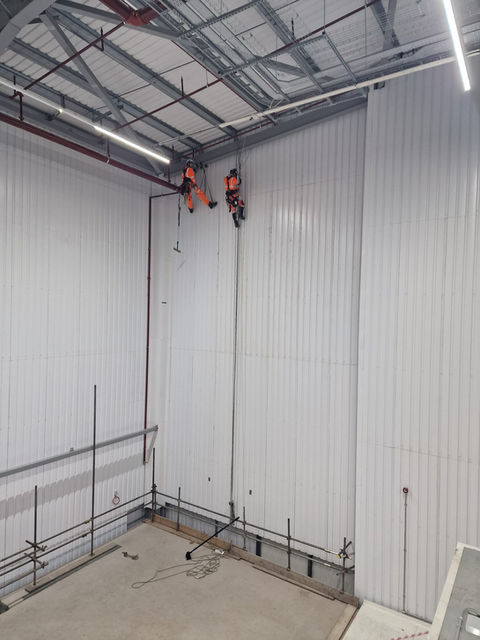 Workers installing white wall panels in a large building.