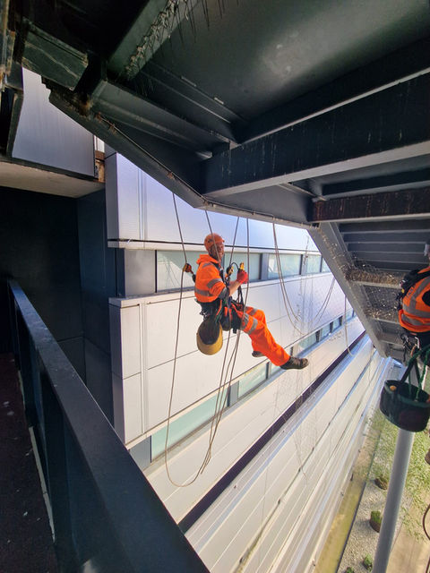 Worker in orange harness rappelling down building