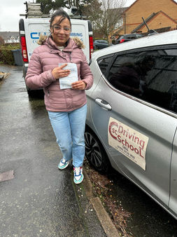 young women stood next to a grey car holding a driving certificate