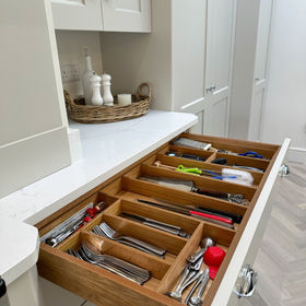 Kitchen drawer with wooden dividers holds organized utensils, including knives and spoons
