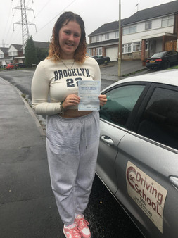 young woman after passing driving test, stood next to a grey car holding a certificate