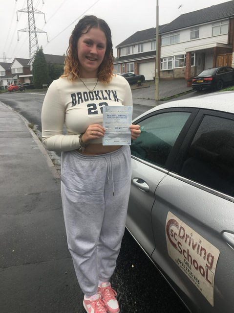 young woman after passing driving test, stood next to a grey car holding a certificate