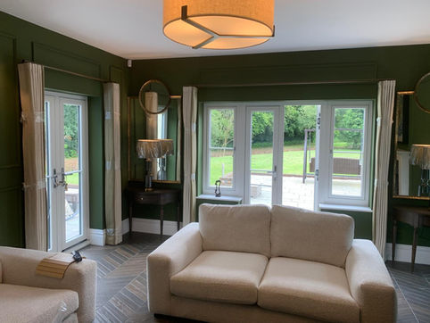 Living room with dark green walls, white sofas, and large windows