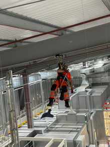 Rope access technician in orange PPE descending over ductwork in an industrial plant