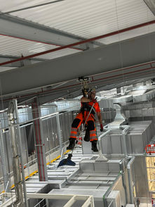 Rope access technician in orange PPE descending over ductwork in an industrial plant
