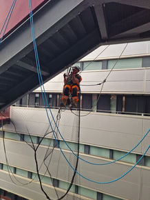 Worker rappelling down building using blue ropes