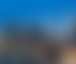 New York City skyline at dusk with illuminated skyscrapers, the Brooklyn Bridge, and waterfront reflections in the East River.