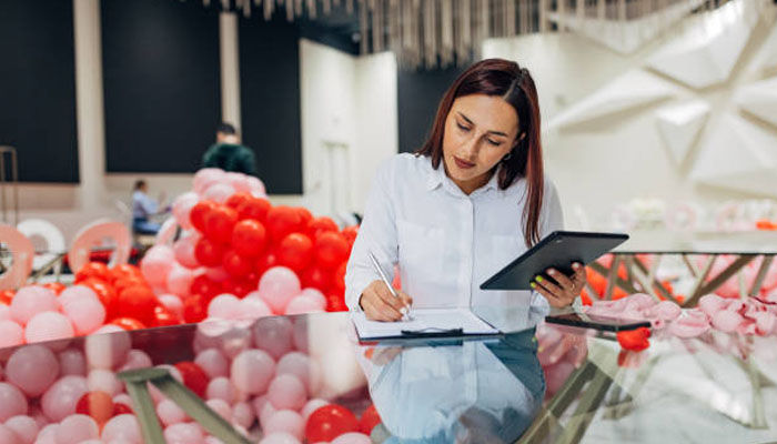 Event planner managing a budget checklist with a tablet during event preparation with colorful decorations in the background