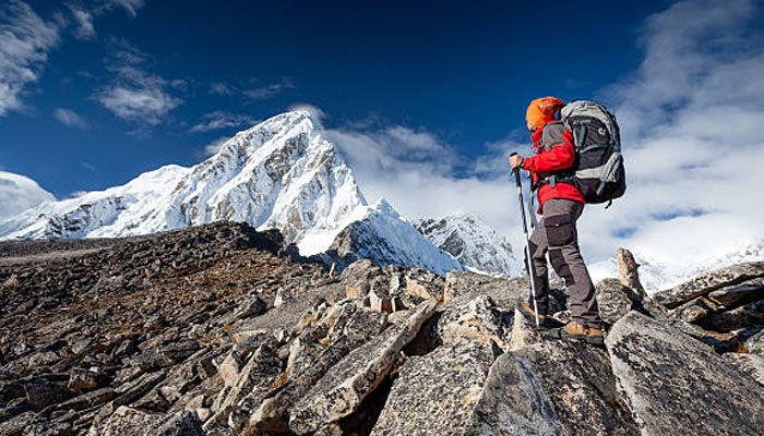 Hiker with a backpack trekking across a rocky mountain trail toward snow-covered peaks, representing hiking business ideas and outdoor adventure.