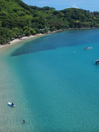 Aerial view of a calm turquoise bay along the Senggigi coastline with lush green hills surrounding the beach.