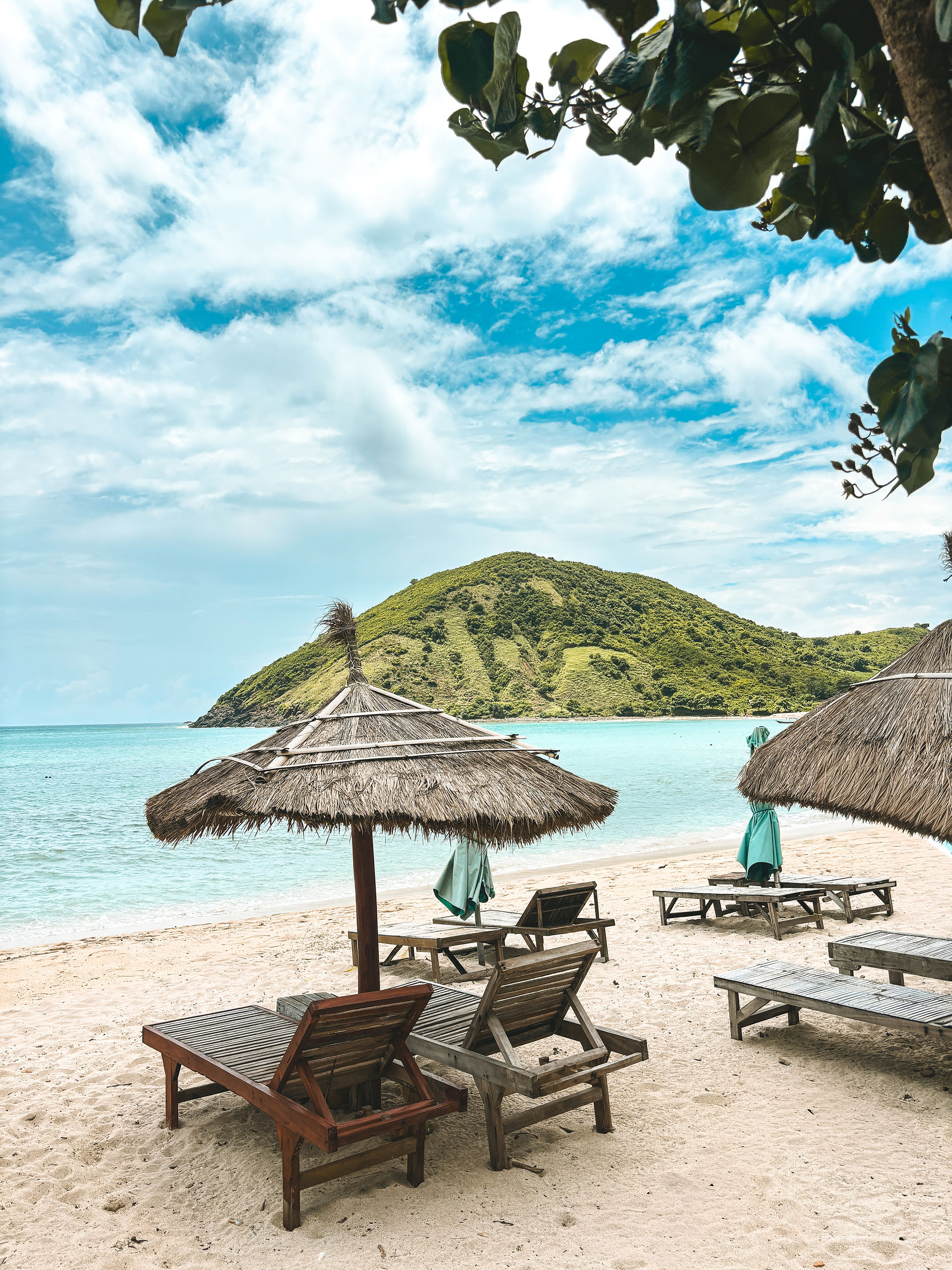 Sun loungers beneath thatched umbrellas overlooking the calm turquoise waters of Mawun Beach in South Lombok.
