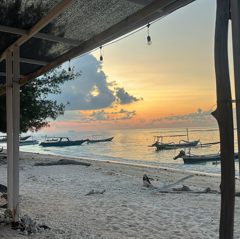 Quiet beachfront on Gili Meno at sunset with traditional boats resting on the sand and calm golden light reflecting across the water.