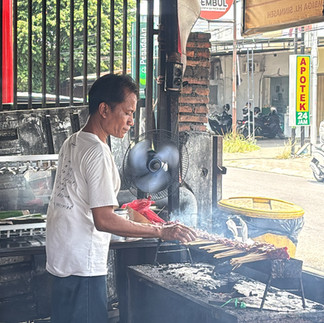 A local vendor grilling traditional satay over charcoal at a street-side stall in Lombok, with smoke rising from freshly cooked skewers.