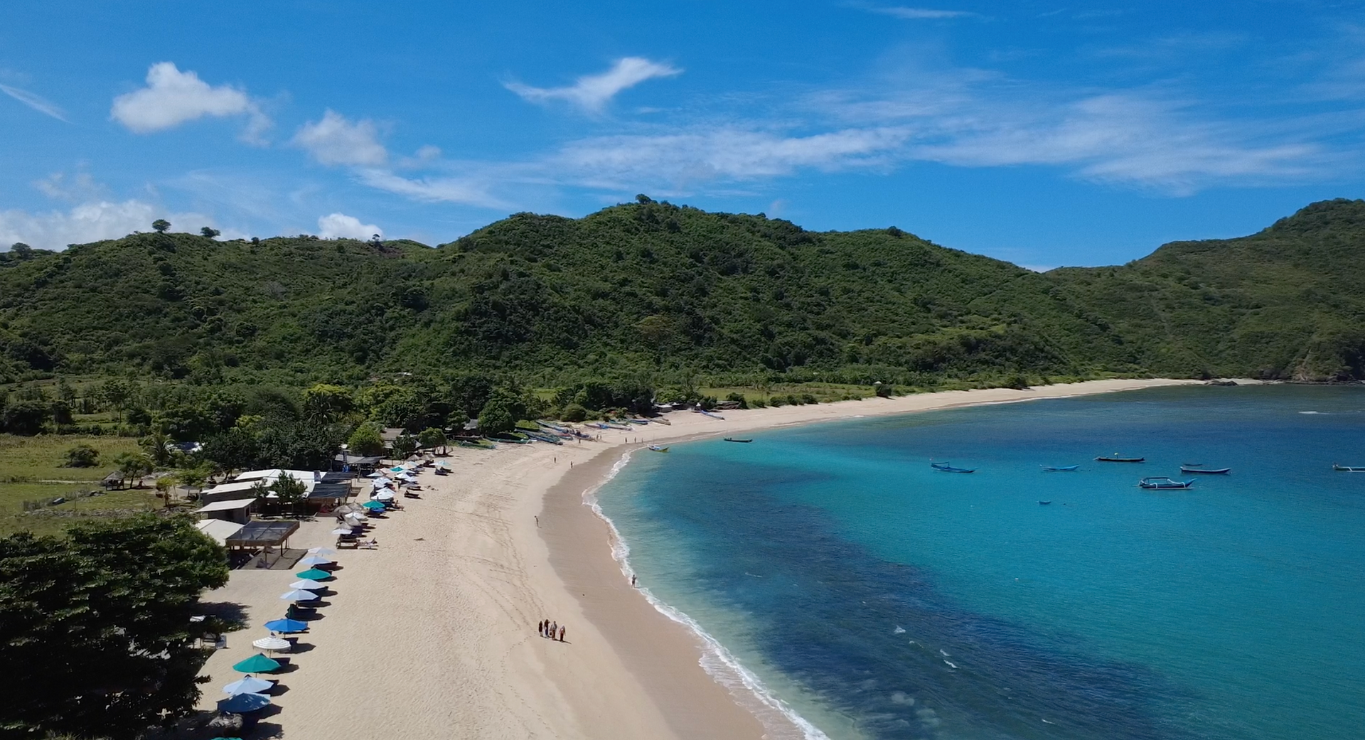 Aerial drone shot of Mawun Beach in South Lombok showing a sheltered crescent bay with calm turquoise water surrounded by lush green hills