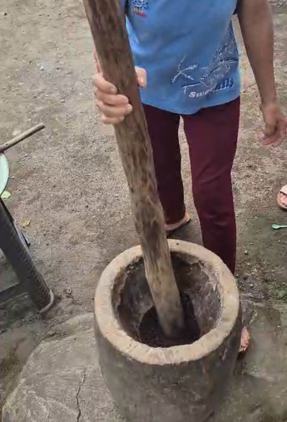 Local woman grinding freshly roasted coffee beans using a traditional wooden pestle and stone mortar in Tetebatu village, Lombok