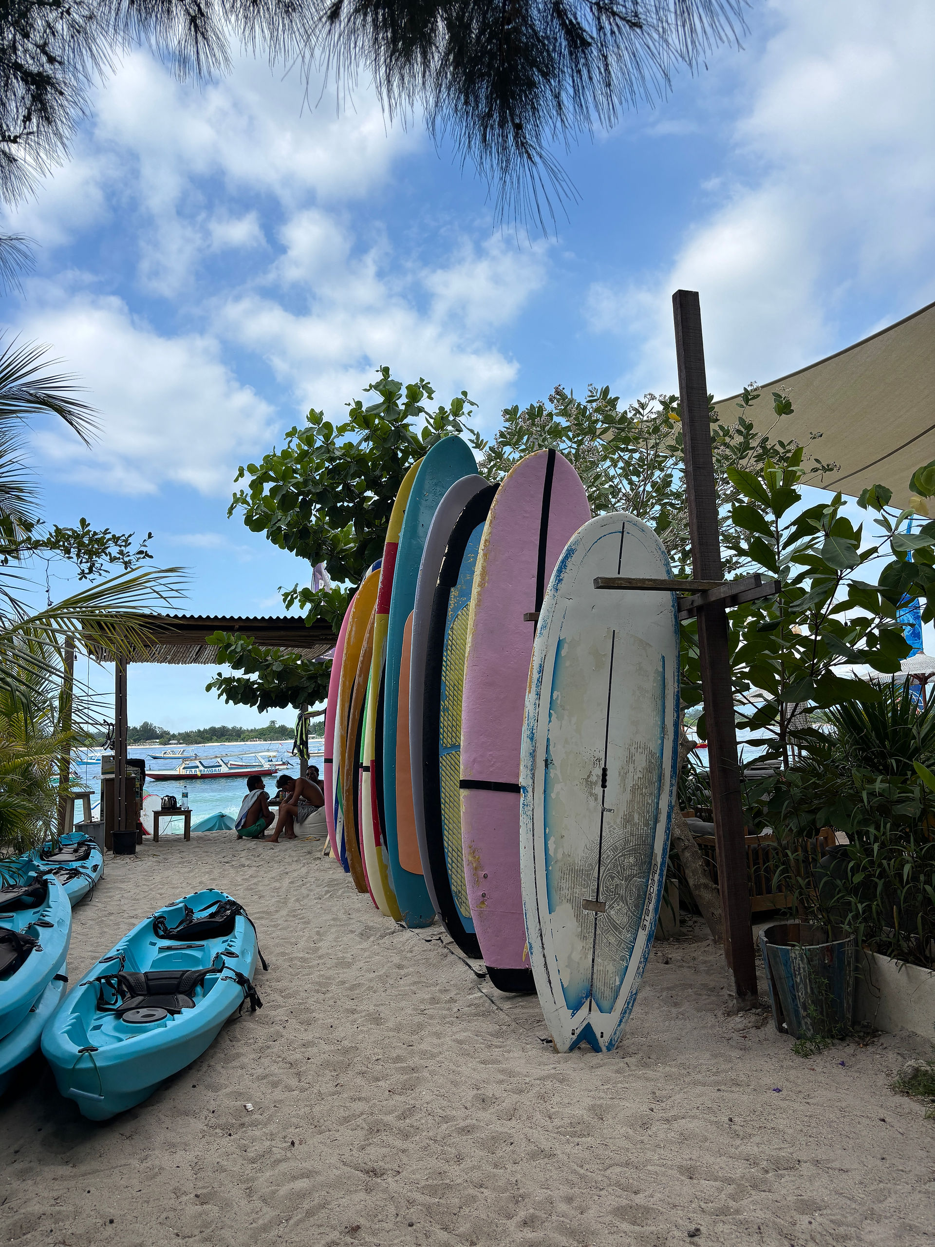 Colorful paddle boards and kayaks lined up along a beachfront in the Gili Islands.