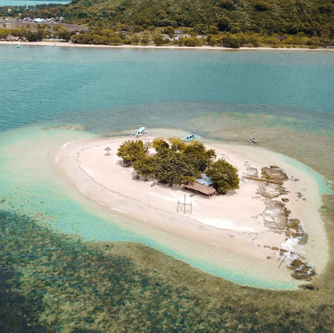 Aerial drone view of a tiny tropical sand island in Lombok’s Secret Gilis surrounded by turquoise water, coral reef, and traditional boats