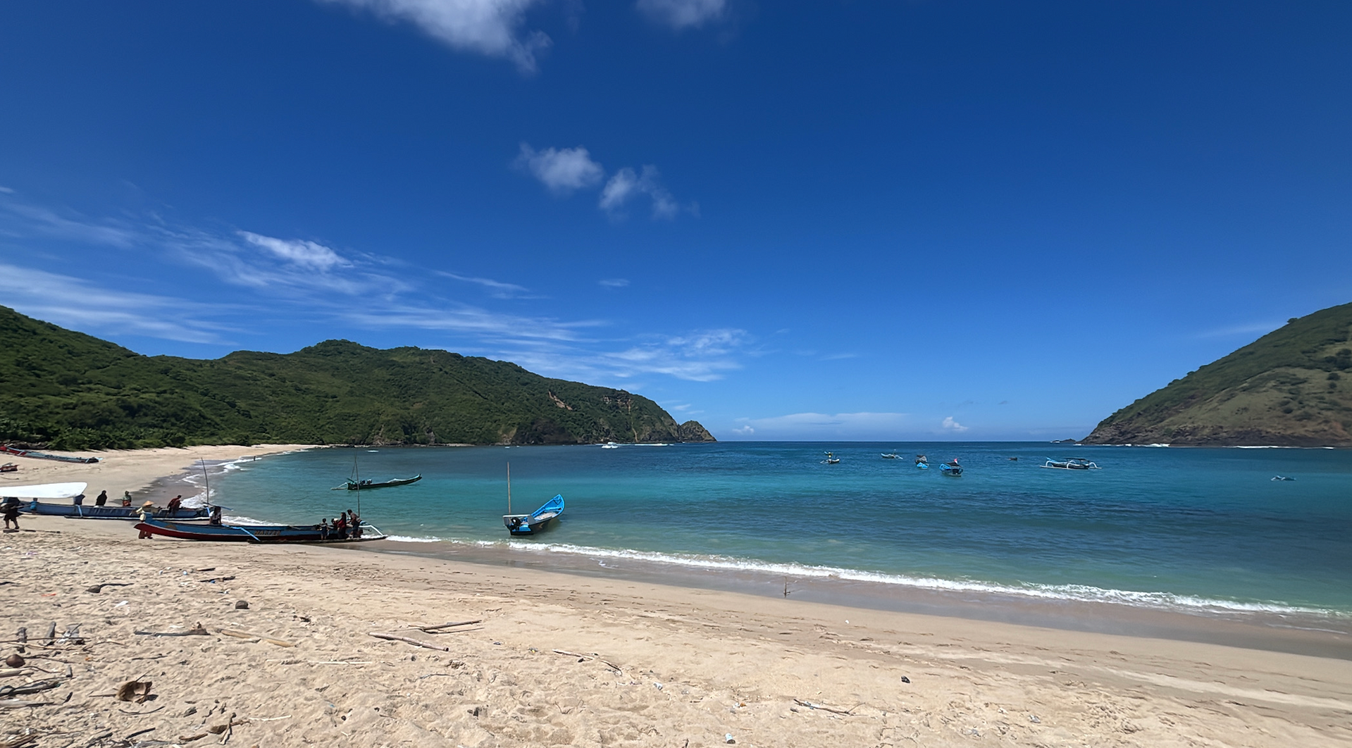 Traditional fishing boats resting on a quiet white sand beach in South Lombok with turquoise water