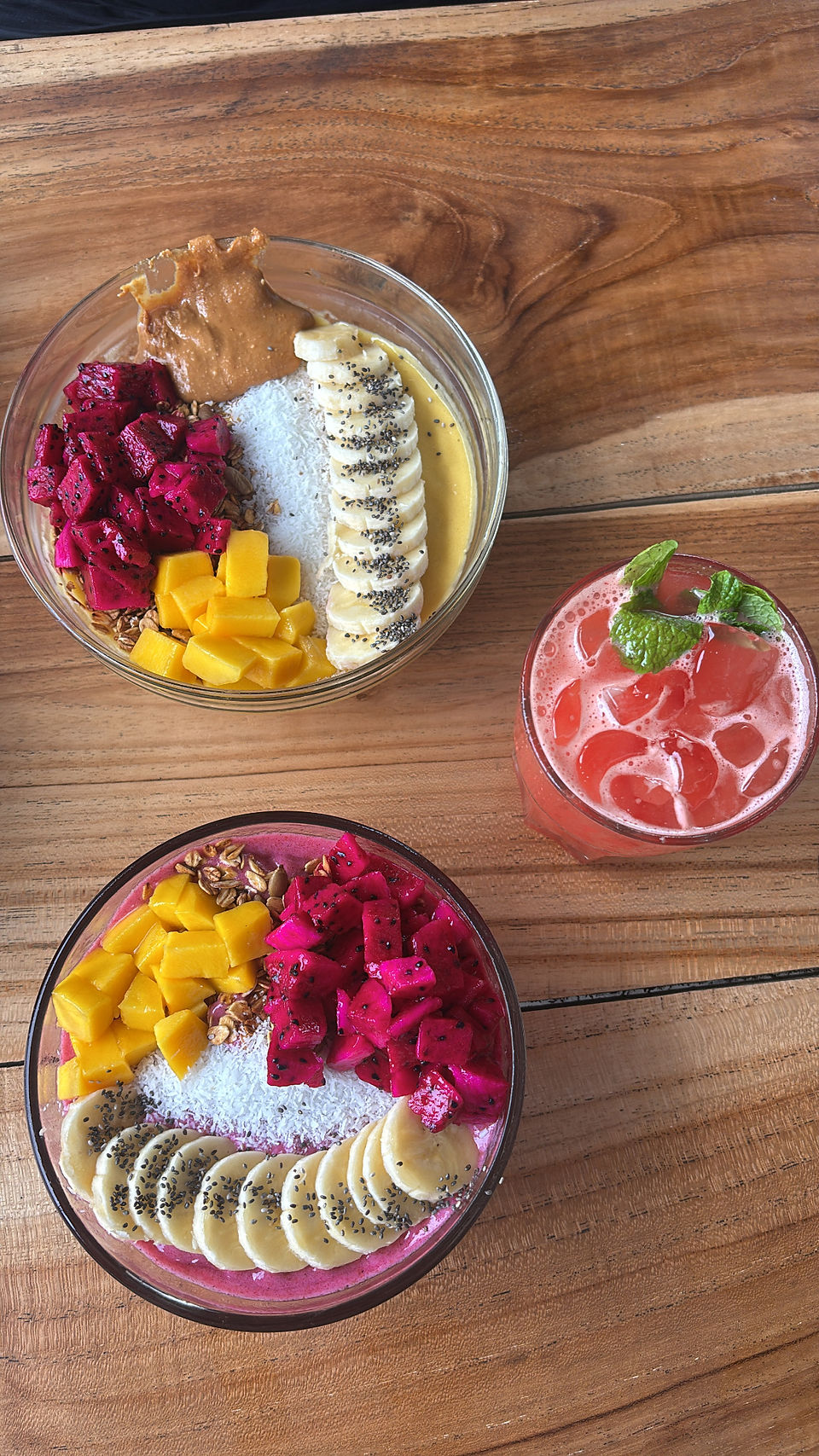 Colorful tropical smoothie bowls topped with mango, dragon fruit, banana, coconut, and seeds beside a pink iced drink.