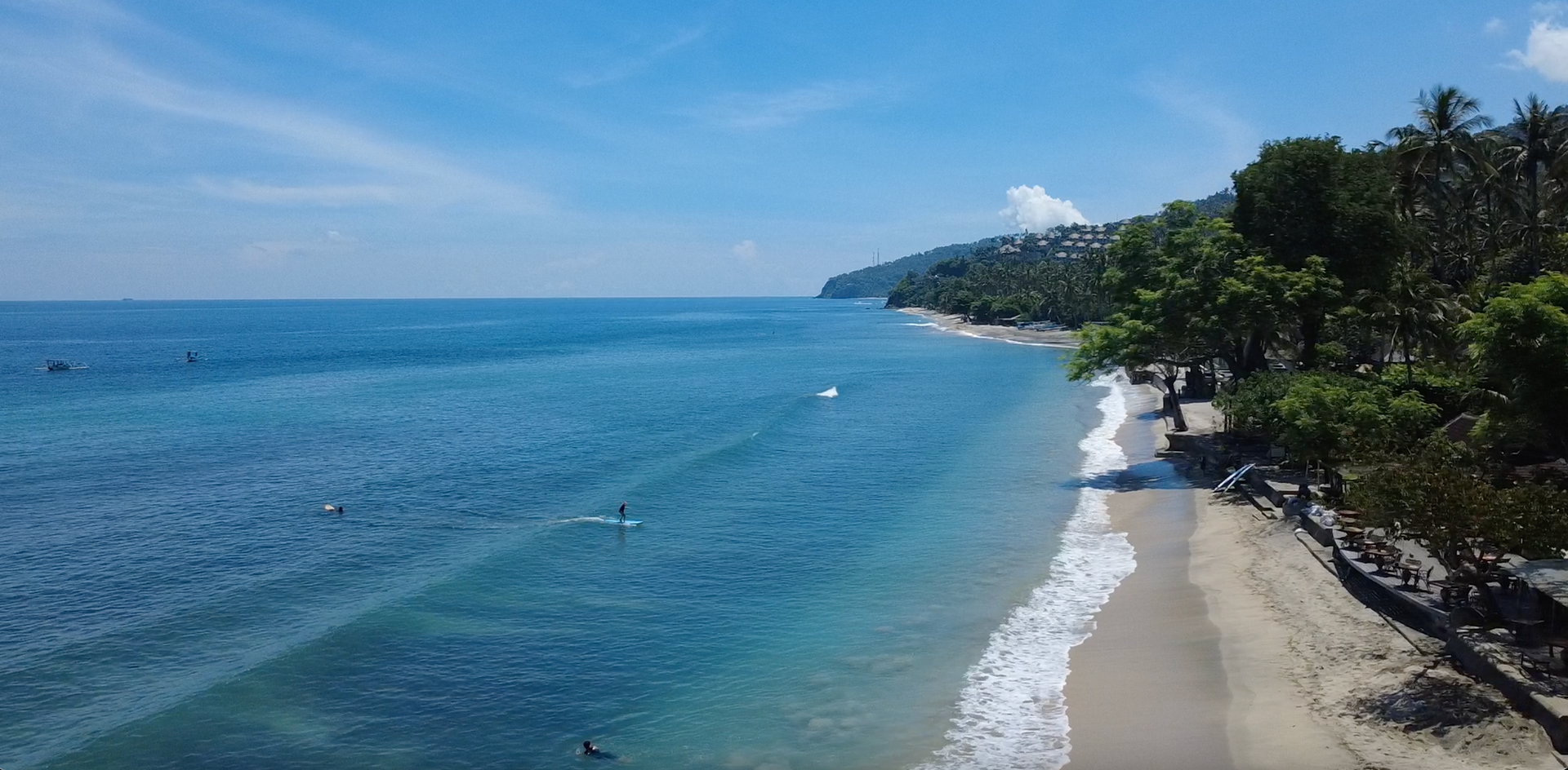 Surfers in the blue water along Senggigi’s palm-lined coastline in West Lombok.